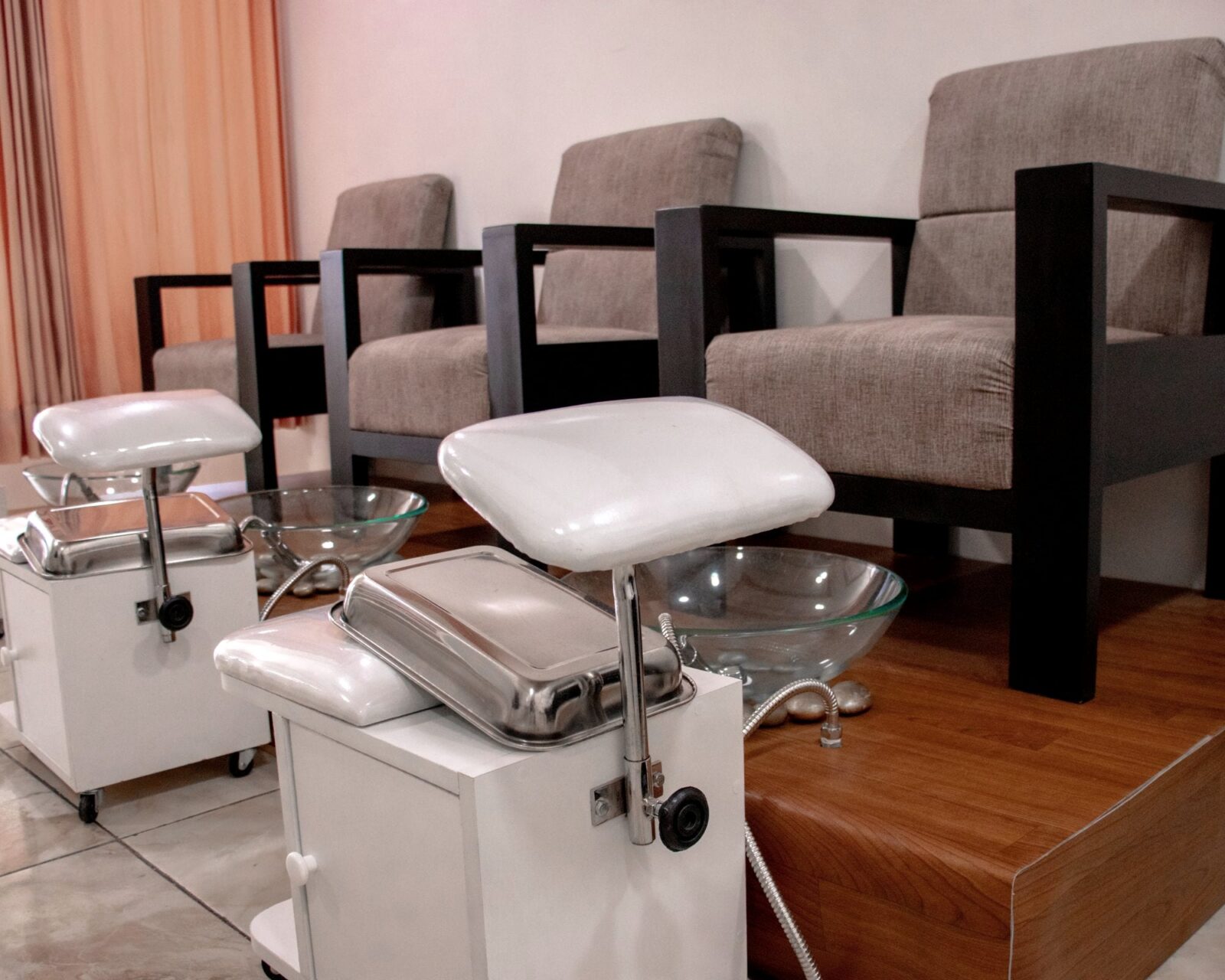 Bright, empty pedicure salon with grey armchairs, glass foot-bath bowls and a warm peach curtain